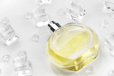 Kadın parfümü sarı şişe, buz küplerinde parfüm şişesinin objektif fotoğrafı ve beyaz masanın üzerindeki su. Yukarıdan bak. Model ürün fotoğrafı, tazelik ve aroma konsepti