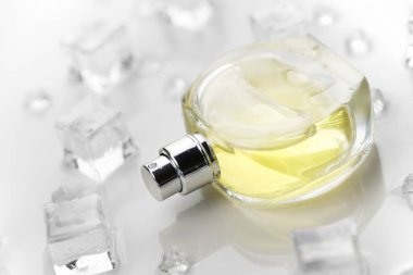 Kadın parfümü sarı şişe, buz küplerinde parfüm şişesinin objektif fotoğrafı ve beyaz masanın üzerindeki su. Yukarıdan bak. Model ürün fotoğrafı, tazelik ve aroma konsepti