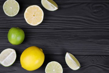 Siyah ahşap masada bir sürü sarı limon ve yeşil limon dilimleri var. Metnin için fotokopi alanı olan taze meyveler mutfakta.
