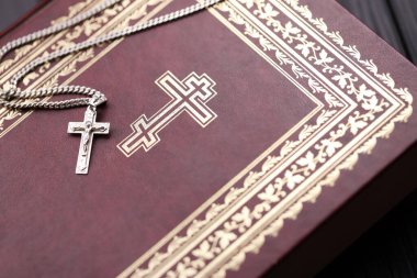 Üzerinde haç olan gümüş kolye siyah ahşap masadaki kutsal Hristiyan kitabının üzerinde. Kutsallığın gücüyle Tanrı 'dan dua etmek, şans getirir ve affedicidir..