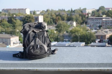 Siyah sırt çantası, güneşli havada, çok katlı bir binanın metal sınırında duruyor.