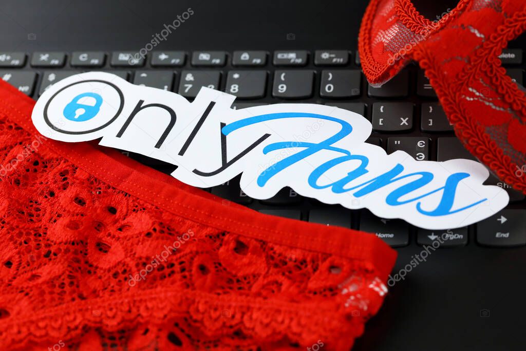 KHARKOV, UKRAINE - FEBRUARY 14, 2021: Onlyfans paper logo and red lingerie on black laptop keyboard. OnlyFans is content subscription service based in London, United Kingdom
