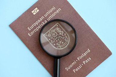 Finlandiya pasaportu ve açık mavi kağıtta büyüteç yakın plan. Vatandaşlık detayları ve bilgi kavramı