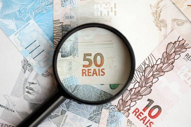 Brezilya reais banknotları ve büyüteç. Mevcut Brezilya gerçek para faturaları ve loupe büyük miktarda masada yatıyor. Brezilya 'da mali izleme ve vergilendirme kavramı