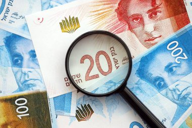 Israel New Shekels banknotları ve büyüteç. Şu anki İsrail 'in yüksek meblağlı faturaları masanın üzerinde yatıyor. İsrail 'de mali izleme ve vergilendirme kavramı