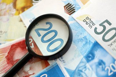 Israel New Shekels banknotları ve büyüteç. Şu anki İsrail 'in yüksek meblağlı faturaları masanın üzerinde yatıyor. İsrail 'de mali izleme ve vergilendirme kavramı