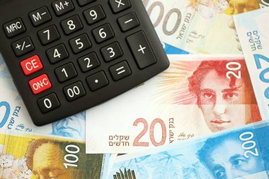 Israel New Shekels banknotları ve hesap makinesi. Mevcut İsrail para faturaları ve kalibreleri büyük miktarda masada yatıyor. İsrail 'de vergilendirme ve para kavramı