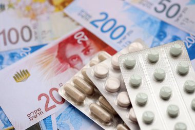 Israel New Shekels banknotları ve ilaç hapları. Mevcut İsrail para ve uyuşturucu faturaları büyük miktarda masada yatıyor. İsrail 'de ilaç ve eczane kavramı