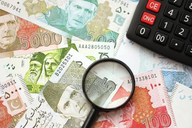 Pakistan banknotları ve büyüteçle hesap makinesi. Mevcut Pakistan para faturaları ve loupe ile calc büyük miktarda masada yatıyor. Pakistan 'da vergi ve para sayımı kavramı