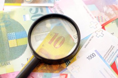 İsviçre frangı banknotları ve büyüteç. İçinde loupe olan şu anki para banknotları büyük miktarda masada yatıyor. İsviçre 'de mali izleme ve vergilendirme kavramı