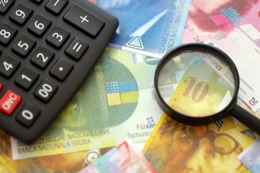 İsviçre frangı banknotları ve büyüteçli hesap makinesi. Mevcut para faturaları ve loupe ile calc büyük miktarda masada yatıyor. İsviçre 'de vergilendirme ve iş kavramı