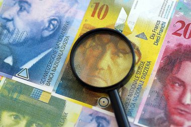 İsviçre frangı banknotları ve büyüteç. Loupe 'un para faturaları büyük miktarda masada duruyor. İsviçre 'de mali izleme ve vergilendirme kavramı