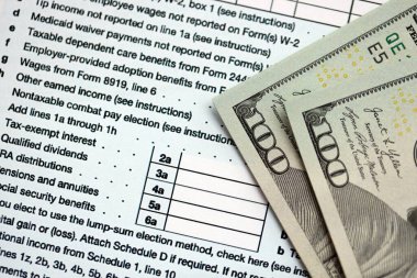 Yüz dolarlık banknotlar ve 1040 bireysel gelir vergisi iade formu yakın çekim. Çok az Amerikan doları ve Birleşik Devletler vergisi yok. ABD 'de vergi ödeme ve muhasebe kavramı