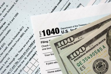 Yüz dolarlık banknotlar ve 1040 bireysel gelir vergisi iade formu yakın çekim. Çok az Amerikan doları ve Birleşik Devletler vergisi yok. ABD 'de vergi ödeme ve muhasebe kavramı