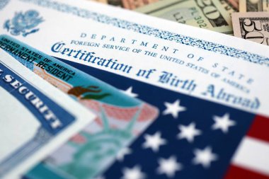 Certification of Birth Abroad with US flag, social security number and Permanent Resident card on US dollar money bills close up