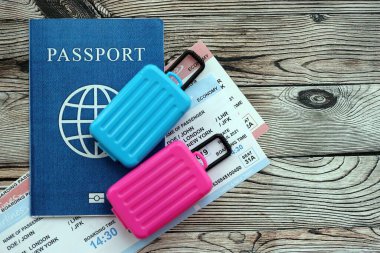 Passport with boarding pass tickets and toy luggage bags on wooden background close up