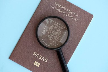 Litvanya pasaportu ve açık mavi kağıtta büyüteç yakın plan. Vatandaşlık detayları ve bilgi kavramı