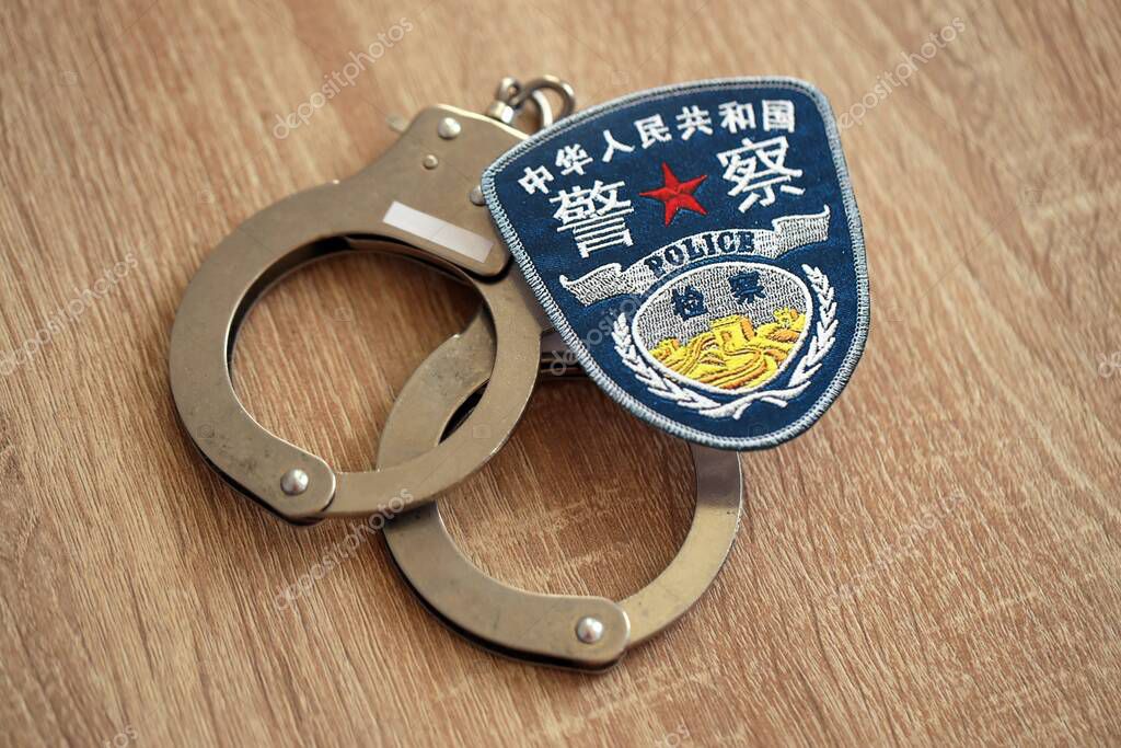 KYIV, UKRAINE - SEPTEMBER 17, 2025 Chinese Police badge with handcuffs on wooden table close up