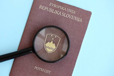 Slovenya pasaportu ve açık mavi kağıtta büyüteç yakın plan. Vatandaşlık detayları ve bilgi kavramı