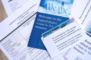 Yeni göçmenler için başvuru ve rehber içeren zarfın içinde daimi oturma izni olan yeşil kart masanın üzerinde.