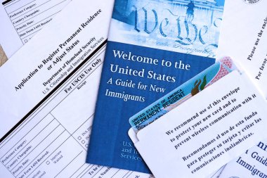 Yeni göçmenler için başvuru ve rehber içeren zarfın içinde daimi oturma izni olan yeşil kart masanın üzerinde.