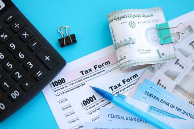 Birleşik Arap Emirlikleri kara para faturaları ve mavi üzerine yakın vergi formlu hesap makinesi. Vergi ve muhasebe kavramı