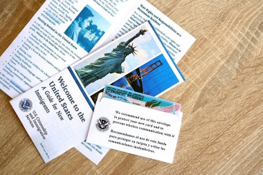 KYIV, UKRAINE - AUGUST 31, 2025 Permanent resident green card in envelope and guide for new immigrants lies on wooden table close up
