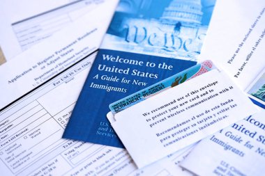 Yeni göçmenler için başvuru ve rehber içeren zarfın içinde daimi oturma izni olan yeşil kart masanın üzerinde.