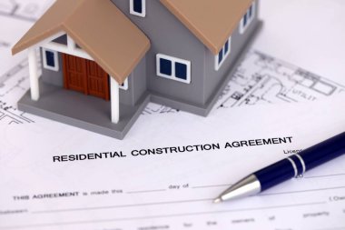 KYIV, UKRAINE - OCTOBER 3, 2025 Residential construction agreement and toy house on white blueprints for construction close up