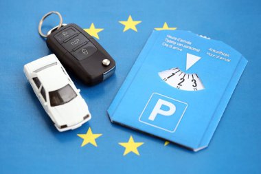 Ön cam için park diski ve Avrupa Birliği bayrağında kontak anahtarı olan beyaz oyuncak araba. Avrupa ülkelerinde sınırlı zaman park sistemi var. Meşgul park alanlarında park süresi kavramı
