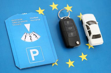 Ön cam için park diski ve Avrupa Birliği bayrağında kontak anahtarı olan beyaz oyuncak araba. Avrupa ülkelerinde sınırlı zaman park sistemi var. Meşgul park alanlarında park süresi kavramı