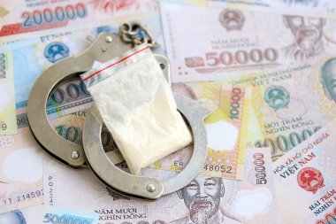 Vietnam dong para birimi faturaları ve kelepçeli kokain paketi. Uyuşturucu suçları kavramı