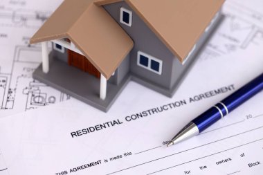 KYIV, UKRAINE - OCTOBER 3, 2025 Residential construction agreement and toy house on white blueprints for construction close up