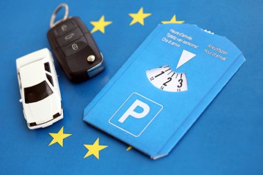 Ön cam için park diski ve Avrupa Birliği bayrağında kontak anahtarı olan beyaz oyuncak araba. Avrupa ülkelerinde sınırlı zaman park sistemi var. Meşgul park alanlarında park süresi kavramı