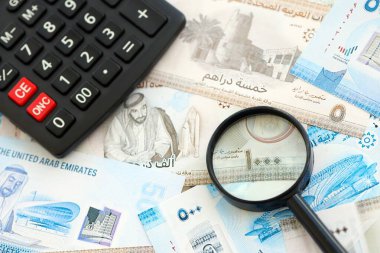Birleşik Arap Emirlikleri kara para birimi faturaları ve büyüteçle yakınlaştırılmış hesap makinesi. Vergilendirme ve para sayımı kavramı