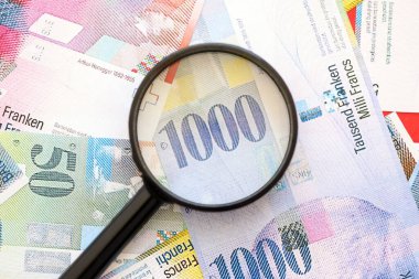 İsviçre frangı banknotları ve büyüteç. İçinde loupe olan şu anki para banknotları büyük miktarda masada yatıyor. İsviçre 'de mali izleme ve vergilendirme kavramı