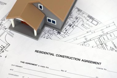 KYIV, UKRAINE - OCTOBER 3, 2025 Residential construction agreement and toy house on white blueprints for construction close up