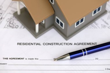 KYIV, UKRAINE - OCTOBER 3, 2025 Residential construction agreement and toy house on white blueprints for construction close up