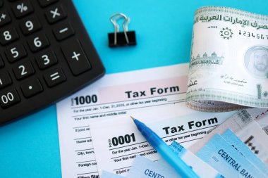 Birleşik Arap Emirlikleri kara para faturaları ve mavi üzerine yakın vergi formlu hesap makinesi. Vergi ve muhasebe kavramı