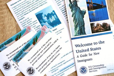 KYIV, UKRAINE - AUGUST 31, 2025 Permanent resident green card in envelope and guide for new immigrants lies on wooden table close up