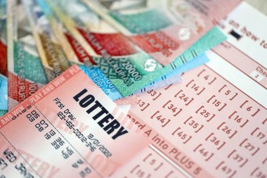 KYIV, UKRAINE - JANUARY 27, 2024 Red lottery ticket lies on pink gambling sheets with indonesian rupiah money bills. Lottery playing concept or gambling addiction in indonesia