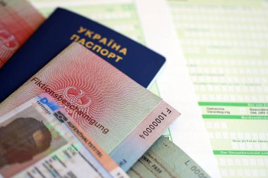 Alman daimi oturma kartı ve belge örneği, vergi formunda Ukrayna pasaportuyla birlikte yakın planda bulunuyor. Aufenthaltstitel ve Fiktionsbescheinung