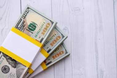 Tahta arka planda üç paket on bin dolarlık banknot. Beyaz tahtalar üzerine yığılmış yüz dolarlık desteler kapanıyor.