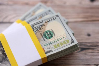 Tahta arka planda üç paket on bin dolarlık banknot. Kahverengi ahşap tahtaların üzerine yığılmış yüz dolarlık desteler kapanıyor.