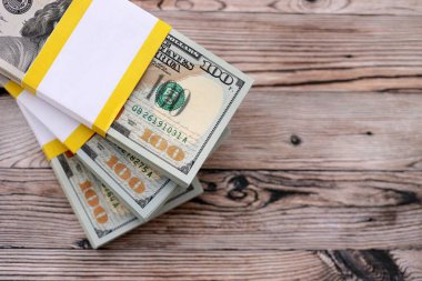 Tahta arka planda üç paket on bin dolarlık banknot. Kahverengi ahşap tahtaların üzerine yığılmış yüz dolarlık desteler kapanıyor.