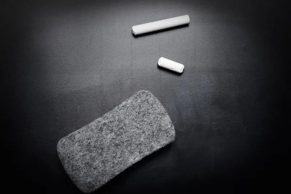 Piece of chalk and eraser on blackboard — Stock Photo, Image