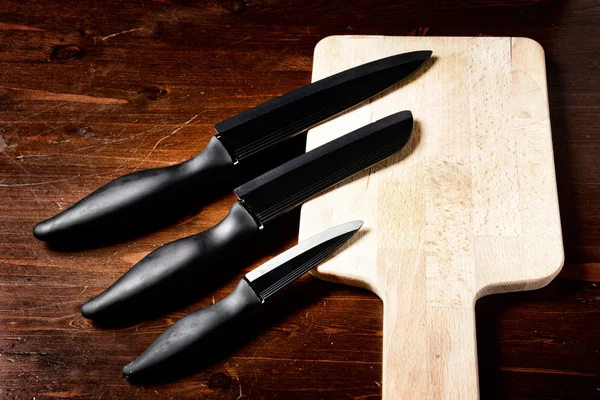 Keskin bıçaklar ve koyu ahşap masa üzerinde kesme tahtası — Stok fotoğraf