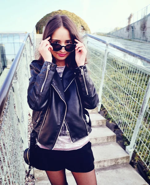 Модель моди в сонцезахисних окулярах і чорній шкіряній куртці позує на відкритому повітрі — стокове фото
