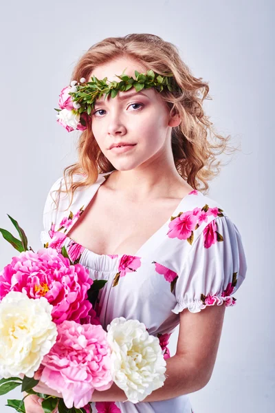 Belleza chica toma hermosas flores en sus manos. Soplando flores. Peinado con flores. Retrato de chica de fantasía en colores pastel. Retrato de hadas de verano. Cabello largo con permanente . — Foto de Stock