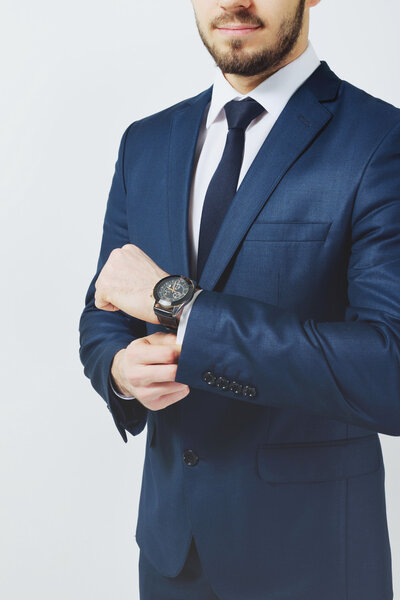 Успешный бизнесмен. Портрет уверенного молодого человека в формальной одежде, смотрящего в камеру и улыбающегося, держа руки скрещенными и стоя на сером фоне
